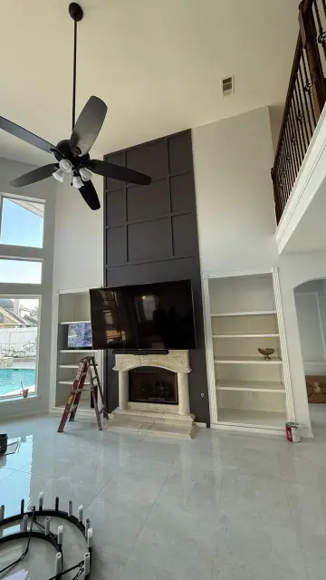 Grand living room with stone fireplace, high ceilings, and engineered hardwood floors overlooking pool – Luxury home remodel Houston TX